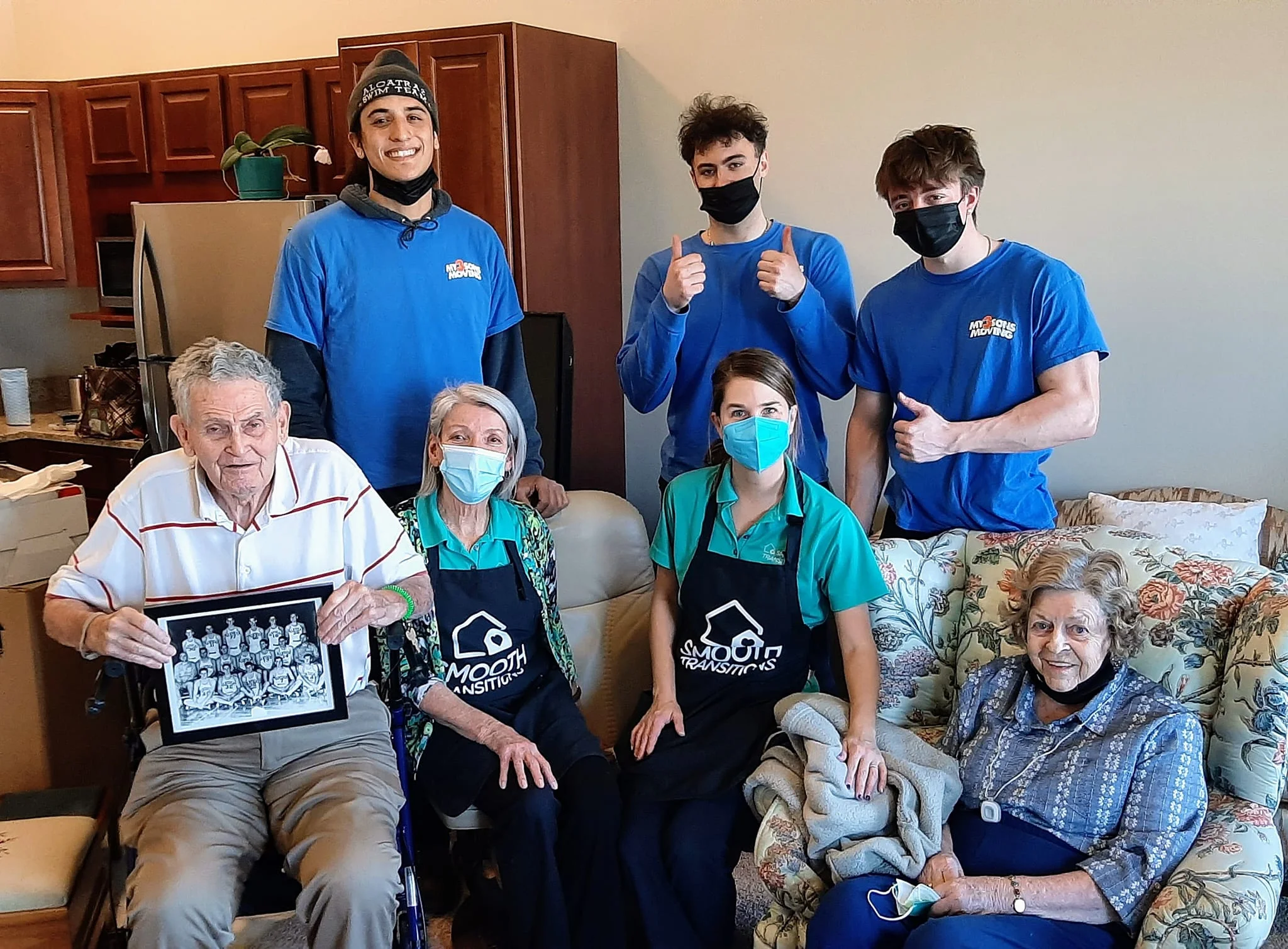 Group of movers and senior living staff posing with three older adults in a living room after an assisted living move.