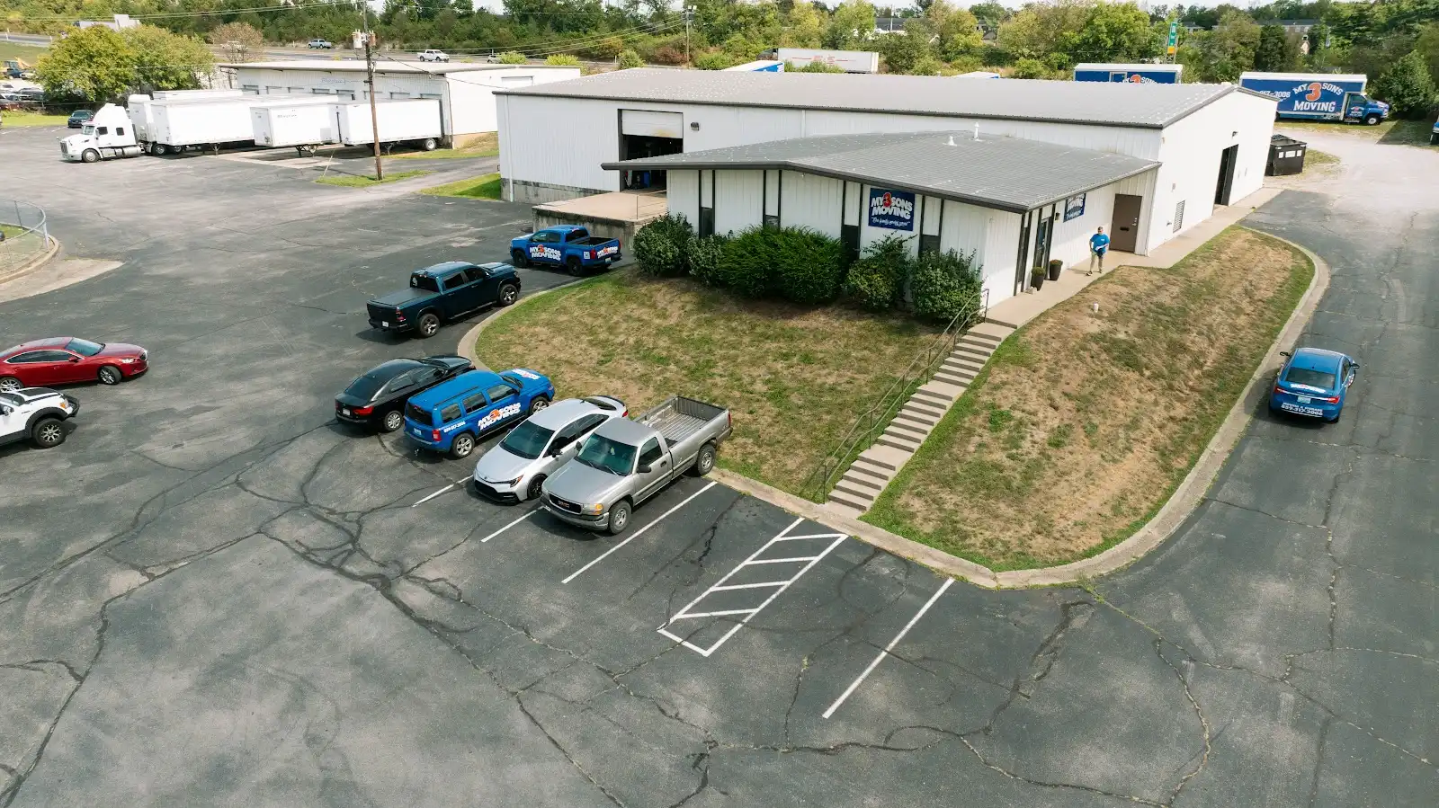 Aerial view of a moving company facility with branded vehicles, warehouse buildings, and parking areas.